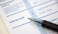 A voter registration form with text saying 'Vote by Mail' and a pen