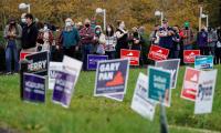 People sand in line to vote behind signs for Glen Youngkin, Terry McAuliffe and others.