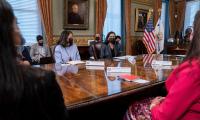 Women wearing masks sit around a large table.
