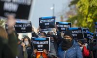 People wearing coats and hats hold signs that say "Voting rights now".