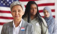 Multi-ethnic group of people at polling station on election day, focus on smiling senior woman with I VOTED sticker looking at camera, copy space
