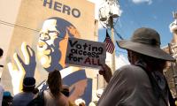A woman holds a sign which says "Voting Access for All" while standing in front of a large mural of John Lewis.