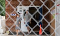 A man and woman exiting a building through double doors seen through a chain link fence.