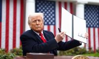 Donald Trump holding up an signed executive order while sitting in front of American flags