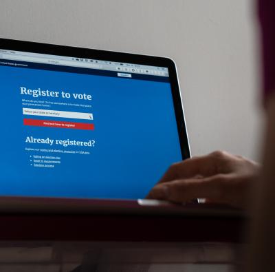 A close up of a laptop screen with a voter registration website and a person's hand on the keyboard.