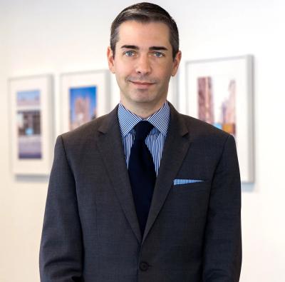 Portrait of Tom Lopach standing in front of a wall with photos on it.
