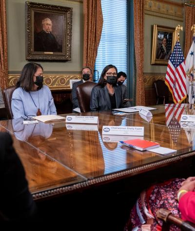 Women wearing masks sit around a large table.