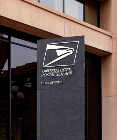 The postal service logo on a sign in front of a building.